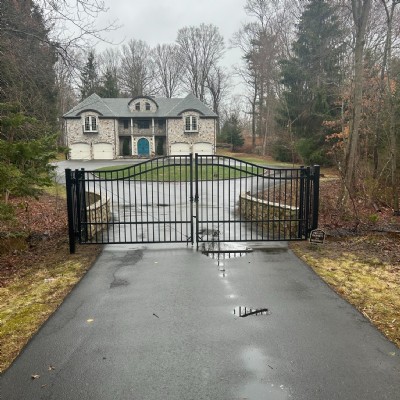 A black metal double swing gate at the entrance to a residential driveway.