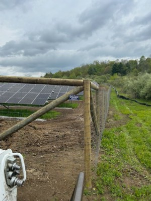 Black wire field fencing secures the perimeter of a solar panel field.