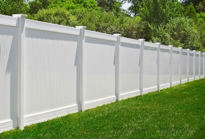 White vinyl fence in yard with green tree leaves in the background